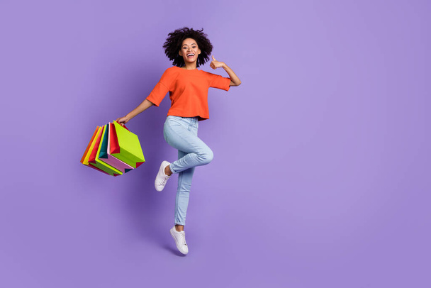 Full size photo of brown haired girl in orange t-shirt and jeans recommend black friday isolated on violet color background - Foto, afbeelding