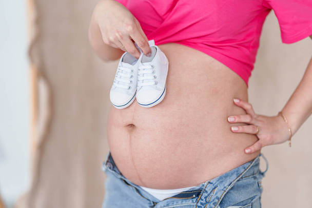 Uma mulher grávida segura os sapatos do bebé na barriga grande. Bela gravidez saudável, esperando o nascimento de um bebê - Foto, Imagem