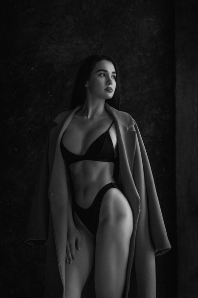 Black and white portrait of attractive young woman in lingerie and coat. Retro soft grain photo effect - Foto, afbeelding