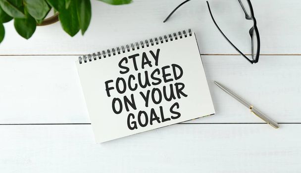 Inspirational quote - Stay focused on your goals. With text message on white paper book, pen, a cup of morning coffee, flower. - Photo, Image