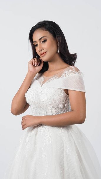 Asian woman in white wedding dress. Thai bride poses before the wedding day. A young woman is happy in a wedding dress. Portrait shot white background in studio. Marriage dress for marriage ceremony. - Φωτογραφία, εικόνα