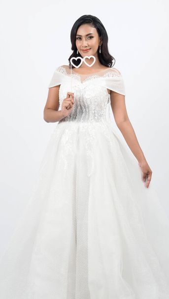 白いウェディングドレスのアジアの女性。結婚式の日の前にタイの花嫁がポーズ。若い女性は結婚式のドレスに満足している。ポートレートはスタジオで白い背景を撮影しました。結婚式のウェディングドレス. - 写真・画像