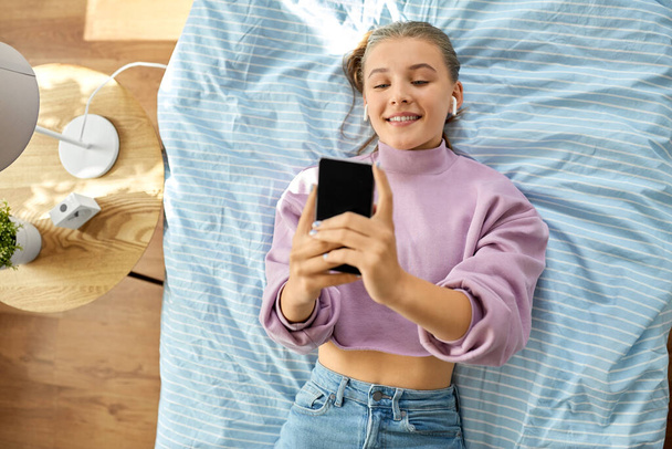 girl in earphones with smartphone lying on bed - Foto, Imagen