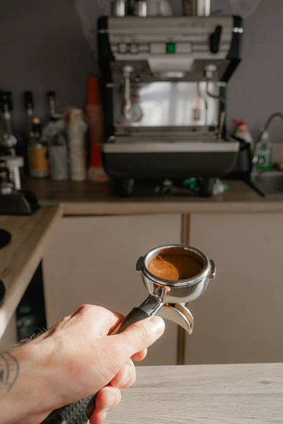 holds a holder with a tempered coffee tablet against the background of a coffee machine, a mini cafe with you, preparing drinks to take away - 写真・画像