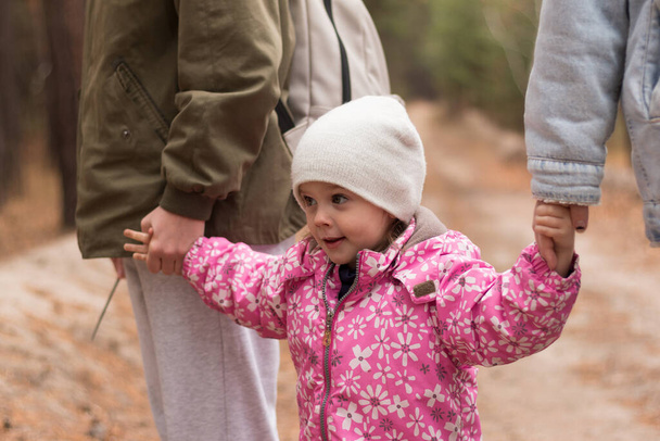 A small child in warm clothes and a hat holds the hands of his parents in his hands on a walk in the park - Foto, Imagen