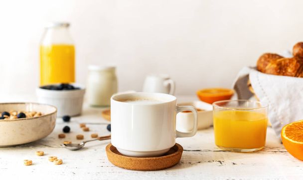 Breakfast concept with cup of coffee, croissants, wholegrain hoops, milk, orange juice, yogurt and blueberries - Foto, imagen