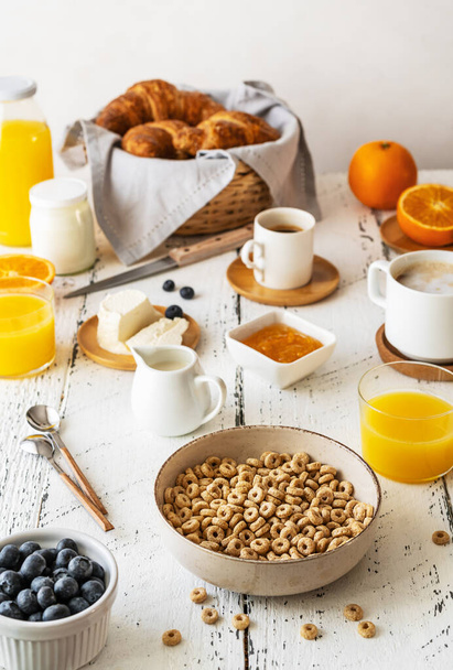 Breakfast concept with cup of coffee, croissants, wholegrain hoops, milk, orange juice, yogurt and blueberries - Photo, image