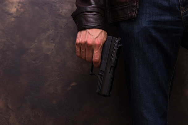 A man in a leather jacket and jeans holding a handgun in his arm - Foto, Bild