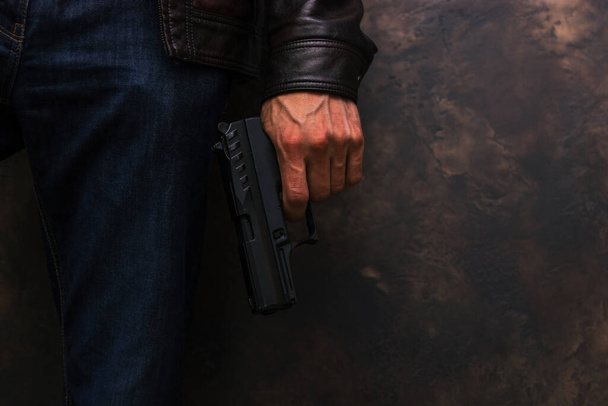 A man in a leather jacket and jeans holding a handgun in his arm - Foto, Bild