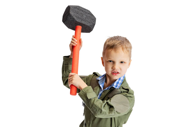 Emotional little boy, cute kid in image of auto mechanic or fitter in green dungarees with work tools isolated over white studio background. Childhood, education concept - Fotoğraf, Görsel