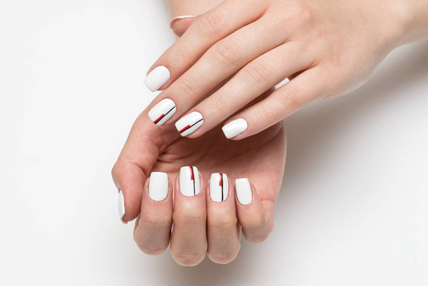 delicada manicura blanca con rayas negro-rojas en clavos cortos cuadrados sobre un fondo blanco de cerca - Foto, Imagen