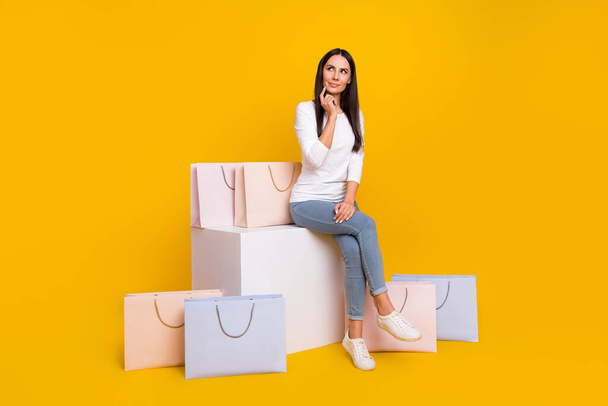 Full size photo of young woman sit platform finger touch chin guess look empty space shopping isolated over yellow color background - Foto, imagen