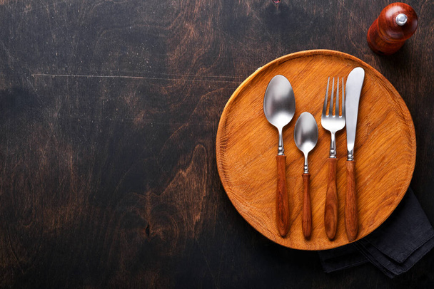 Vintage silverware. Rustic vintage set of wooden spoon and fork on wooden platter on black wooden background. Empty dishes. Top view. Mock up. - Foto, afbeelding