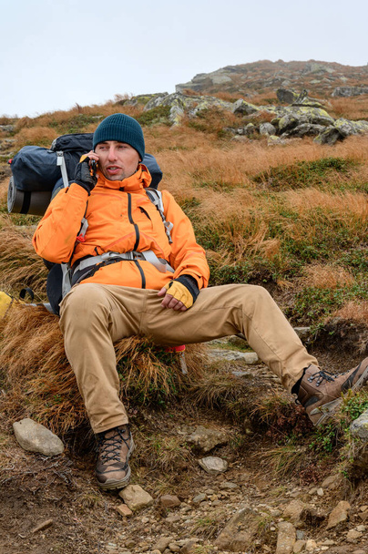 Мужчина разговаривает по телефону в горах, мобильная сеть и связи в горах, мобильная связь в горах, турист с большим рюкзаком. - Фото, изображение