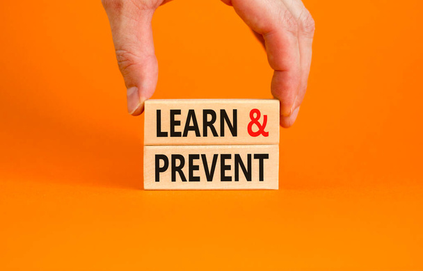 Learn and prevent symbol. Concept words Learn and prevent on wooden blocks on a beautiful orange table orange background. Businessman hand. Business learning and learn and prevent concept, copy space. - Photo, Image
