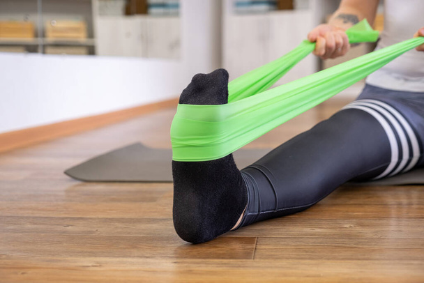 dívka protahuje nohu s elastickým proužkem ve fitness místnosti - Fotografie, Obrázek