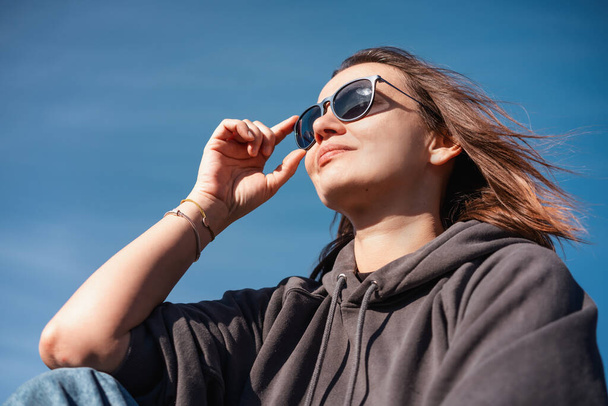 Portrait of a young adult woman in sunglasses against a blue sky - Foto, Imagem