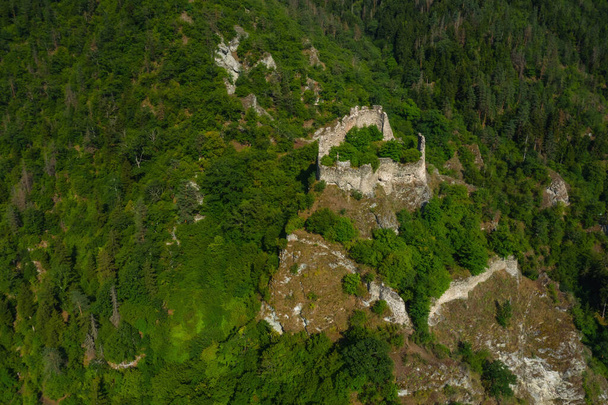 I resti di un'antica fortezza sulle montagne della località turistica di Borjomi in Georgia. Un antico castello in rovina in Georgia. Veduta aerea di verdi catene montuose e piste in estate - Foto, immagini