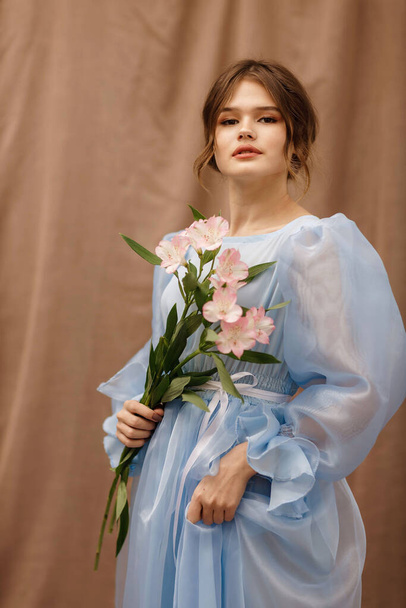 a girl in a blue dress with flowers in her hands - Foto, afbeelding