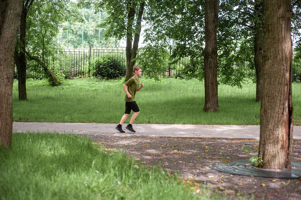 A teenage boy plays sports. Running training. Morning jog through the summer park. Healthy lifestyle. Hobbies of teenagers. - Fotó, kép