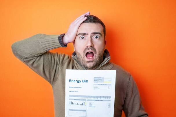 Choqué homme lisant quelques factures dépenses d'énergie isolé sur fond orange - Photo, image