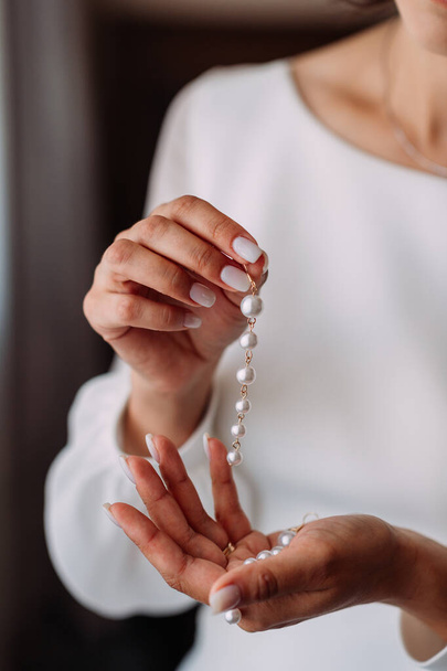 Una chica en blanco sostiene largos pendientes de perlas en sus palmas. - Foto, imagen