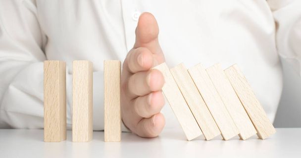Close up of businessman hand Stopping Falling wooden Dominoes effect from continuous toppled or risk, strategy and successful intervention concept for business. - Foto, Bild