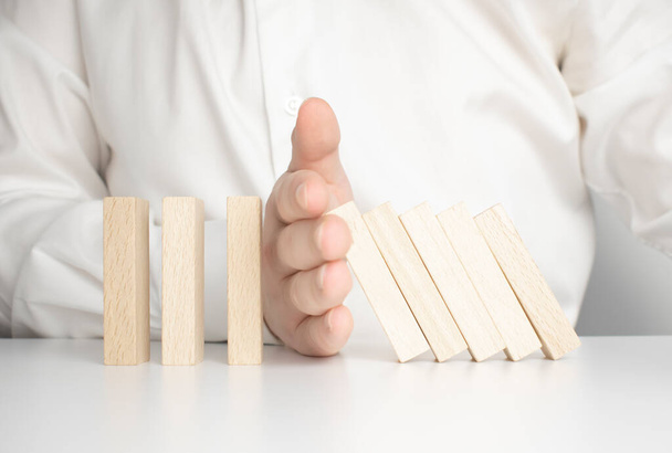 The concept of stopping the crisis. Hand holds wooden blocks on a blue background. Close up. - 写真・画像