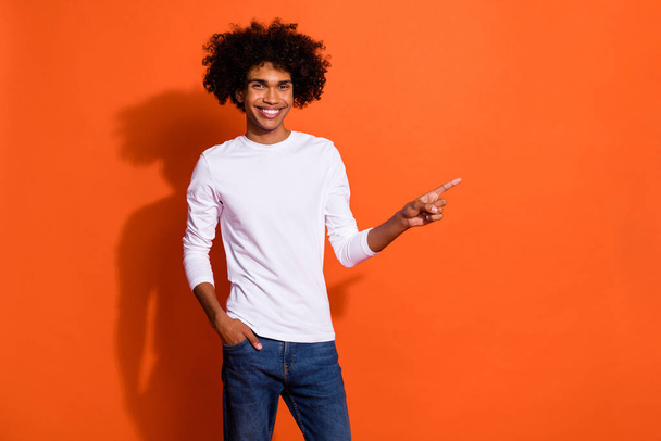 Photo of sweet charming guy wear white shirt pointing finger empty space isolated orange color background - Fotó, kép