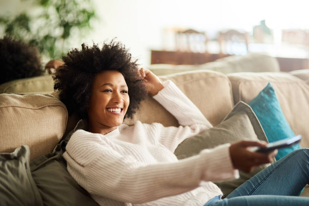 De permiso hasta nuevo aviso. Foto de una joven mujer relajándose en el sofá en casa y viendo la televisión. - Foto, imagen