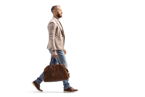 Full length profile shot of a man in a beige suit and jeans carrying a fashionable bag isolated on white background - Foto, imagen