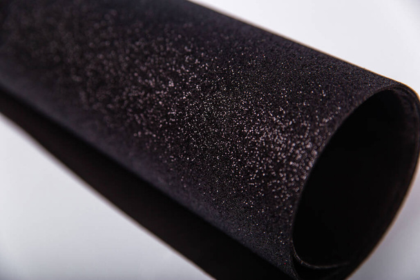 A roll of thick black paper with sparkles on a white background. Shiny fabric for creativity. Isolate - Foto, Imagen