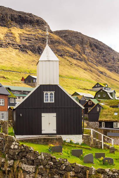 Näkymä puinen kirkko Bour Vagar saarella. Pieni kylä sijaitsee rinteessä kukkulalla. Färsaaret. - Valokuva, kuva