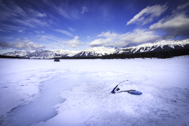 Caña de pescar sobre hielo y cabaña de pesca distante montada en un lago de montaña congelado en Kananaskis Alberta Canadá. - Foto, imagen