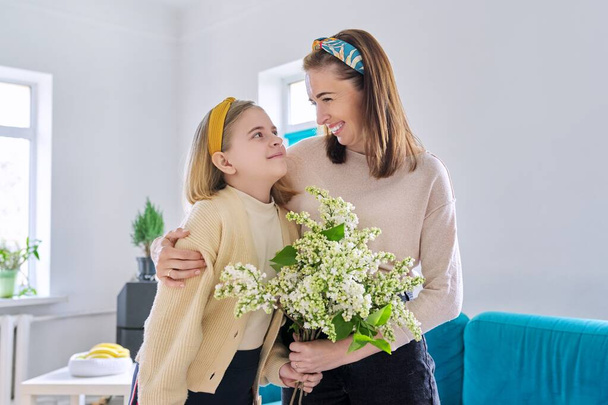 Happy mother and daughter child congratulating with bouquet of flowers and hand-drawn card, at home in living room. Mothers day, family, relationship, emotions, love, togetherness concept - Φωτογραφία, εικόνα