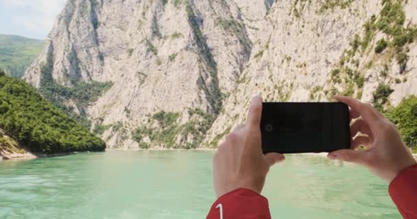meisjes handen, houd een smartphone vast en maak foto 's van de schoonheid van het meer, fjord in Albanië, Drin, Komani. Heldere dag, uitzicht vanaf de veerboot. Hoge kwaliteit 4k beeldmateriaal - Video