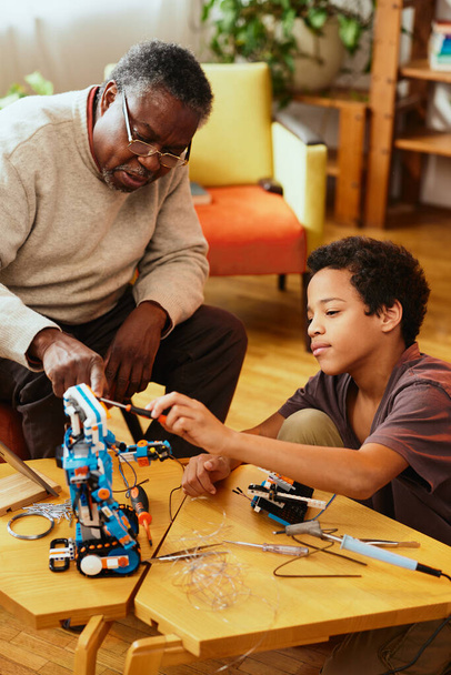 Um avô e um neto a fazer um robô juntos em casa. Educação em robótica e eletrônica. - Foto, Imagem