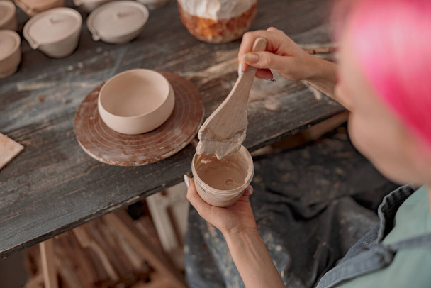 Vue en angle élevé de la jeune femme plongeant le pinceau dans la peinture acrylique tout en décorant le plat de poterie dans l'atelier de céramique - Photo, image