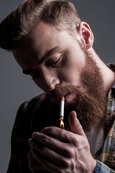 Young bearded man lighting up a cigarette - Foto, Imagen