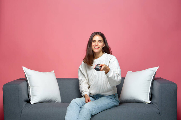 Smiling girl holding tv remote controller, sitting on couch, watching movie at home, spending leisure time with television. High quality photo - Valokuva, kuva