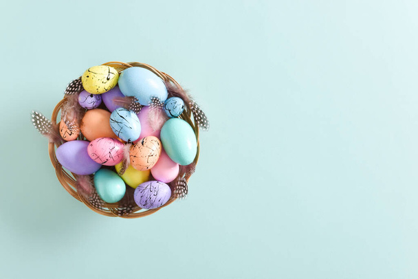 Paskalya kartı. Minimalizm. Boyanmış Paskalya yumurtaları ve tüyleri olan bir yuva. Uzayı kopyala Düz yatış, üst görünüm. - Fotoğraf, Görsel