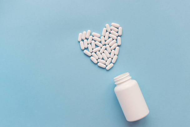 心臓の形をした白い丸薬と青い背景の白い瓶。心臓の健康のための薬。医療・ヘルスケアの概念 - 写真・画像