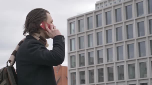 Stijlvolle jongeman in sjaal en zwarte jas die per mobiele telefoon praat op de straat van Wroclaw, Polen - Video