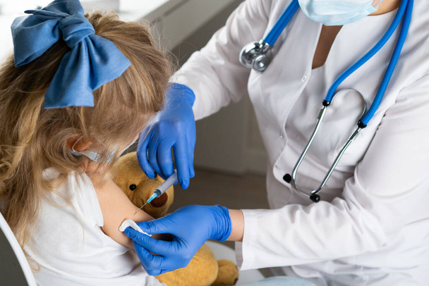 vaccinatie van kinderen, een klein meisje bij een doktersafspraak, een injectie in de arm, de conce. - Foto, afbeelding