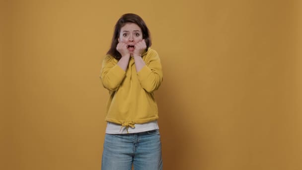Portret van een vrouw die bang is en handgebaar maakt en haar gezicht aanraakt in angst, bang en bang over een gele achtergrond. Jongeren doen geschokt gezicht grimas wordt opgeschrikt in de studio. - Video
