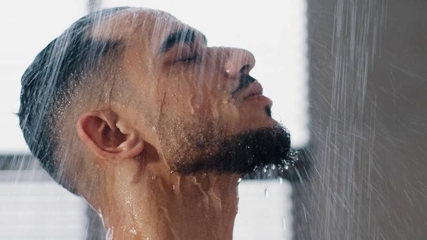Sexy verführerischen arabischen bärtigen Mann in Duschkopf Duschen im Badezimmer zu Hause in Großaufnahme. Millennial Brünette Kerl Spülung Shampoo und Conditioner aus den Haaren in warmem Bad heißes Wasser läuft Gesicht hinunter - Foto, Bild