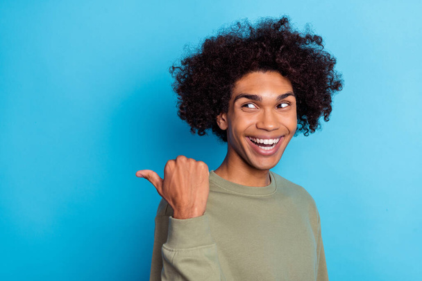 Photo of young cheerful man look indicate finger empty space promotion proposition isolated over blue color background. - 写真・画像