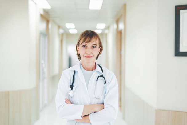 Portrait of caucasian senior woman doctor posing with arms crossed with stethoscope in hospital - Zdjęcie, obraz