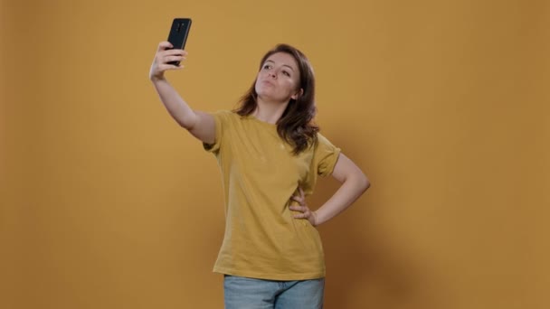 Portret van een vrouw die smartphone gebruikt om een selfie gevoel vol vertrouwen en mooie opvallende meerdere poses in de studio te nemen. Persoon die mobiele telefoon gebruikt om foto 's te maken met behulp van camera om te posten op sociale media. - Video