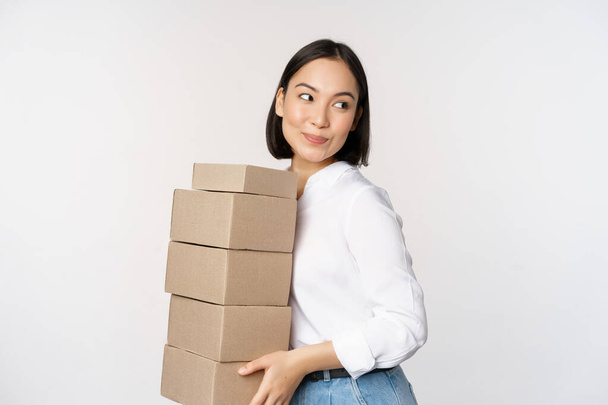 Nuoren aasialaisen naisen muotokuva, jolla on laatikoita, kuljettaa tavaraa. Korealainen naisyrittäjä koota järjestys, pysyvän voer valkoinen tausta. - Valokuva, kuva